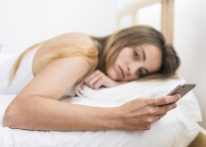 young-woman-lying-on-bed-using-mobile-phone